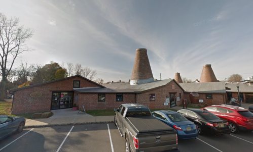 A brick building with large chimneys, surrounded by parked cars and trees under a cloudy sky.