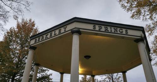 A gazebo with the words "Berkeley Springs" displayed prominently on its roof, surrounded by trees in autumn.