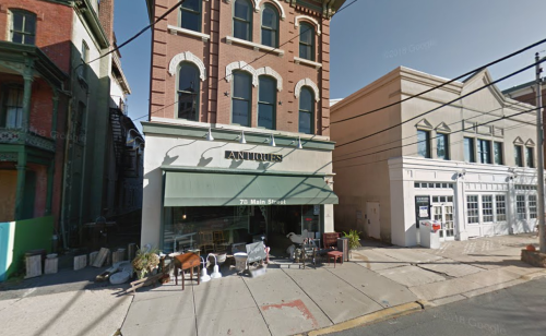 A street view of an antique shop with outdoor furniture displays and neighboring buildings on a sunny day.