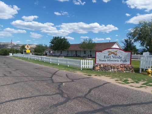 Sign for Fort Verde State Historic Park with a white picket fence and a clear blue sky in the background.