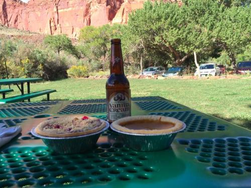 A picnic table with two pies and a bottle of vanilla cream soda, set against a backdrop of red rock formations and greenery.