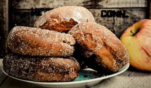 A plate of sugar-coated donuts next to a fresh apple, set against a rustic wooden background.
