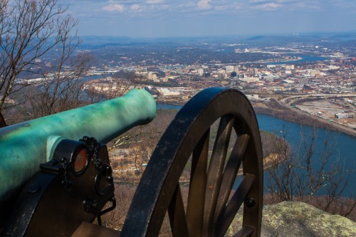 A historic cannon overlooks a cityscape and river from a high vantage point on a clear day.