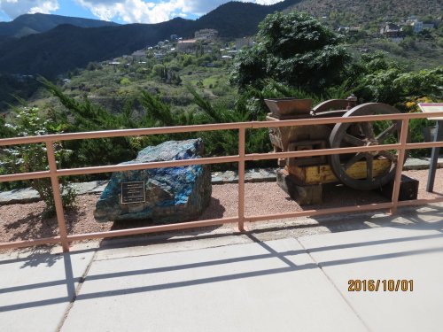 A large rock with a plaque beside an old mining equipment display, set against a mountainous landscape.