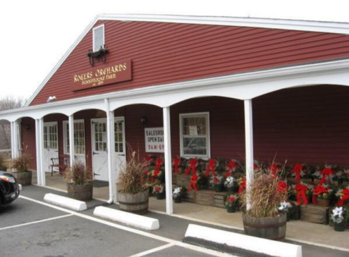 A red barn-style building with white trim, featuring flower pots and holiday decorations outside.