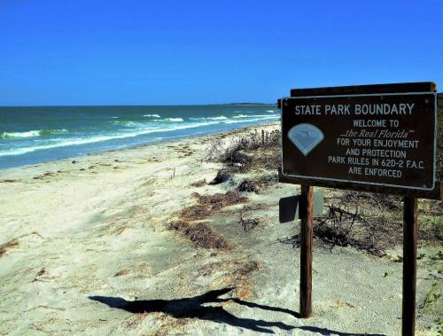 A sandy beach with gentle waves and a sign marking the state park boundary under a clear blue sky.