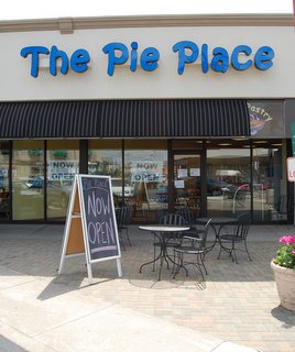 Exterior of "The Pie Place" with a sign reading "Now Open" and outdoor seating.