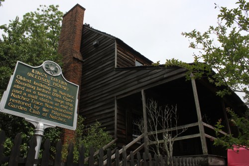 Historic building with a wooden structure, sign reading "King's Tavern (Gledso House)" in front, surrounded by greenery.