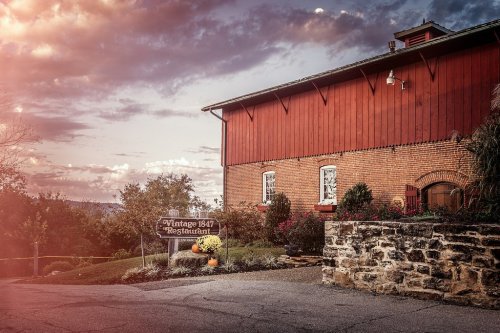 A rustic red barn with a sign for "Vintage 1847 Restaurant," surrounded by greenery and a scenic sky.
