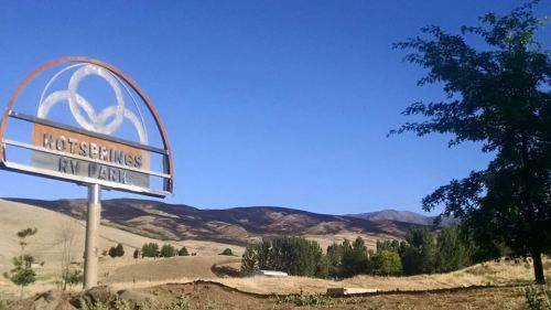 Sign for "Hot Springs RV Park" with rolling hills and a clear blue sky in the background.