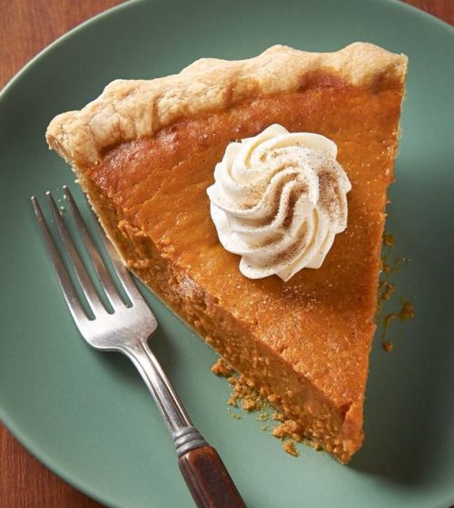 A slice of pumpkin pie topped with whipped cream on a green plate, with a fork beside it.