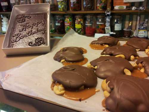 A tray of chocolate-covered treats with caramel and nuts, next to a box that says "Happy Birthday."