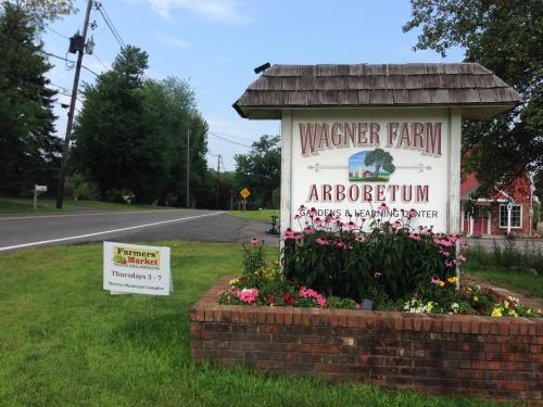 Sign for Wagner Farm Arboretum with flowers in front, located by a road, featuring a nearby farmers market sign.