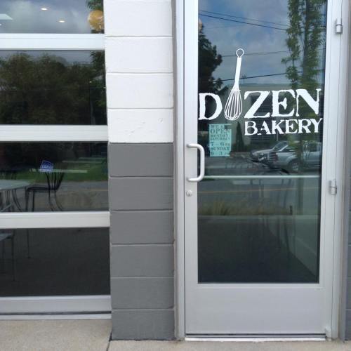 A bakery entrance with a glass door and a sign that reads "Dozen Bakery" featuring a whisk graphic.