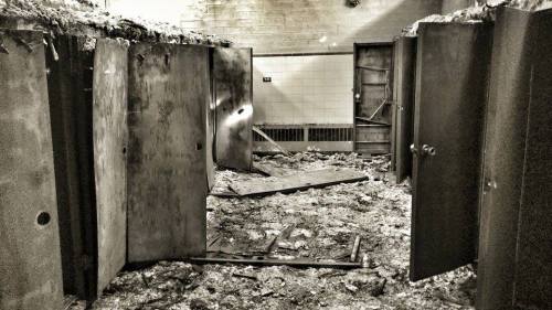 Abandoned room with open metal doors and debris scattered on the floor, suggesting decay and neglect.