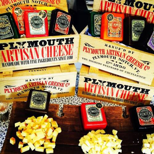 Display of Plymouth Artisan Cheese products, featuring various flavors and blocks of cheese on a rustic table.