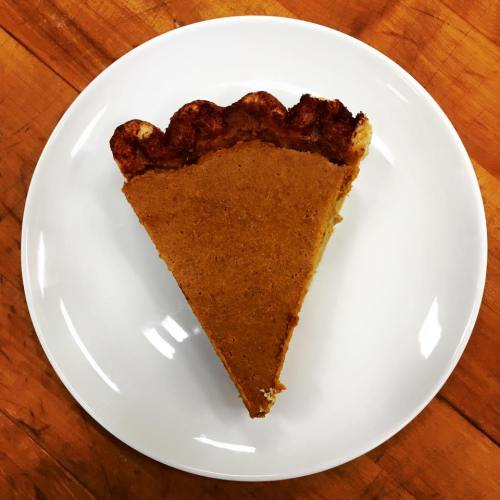 A slice of pumpkin pie on a white plate, resting on a wooden surface.
