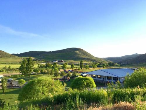 A scenic view of rolling hills, green trees, and a building in a peaceful landscape under a clear blue sky.