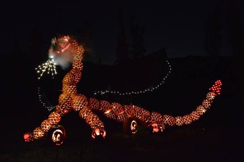A large, illuminated dragon sculpture made of glowing orbs, with smoke and lights, set against a dark background.