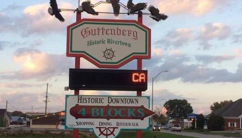 Sign for Guttenberg, Historic Rivertown, featuring a digital display and birds flying above, with directions to downtown.