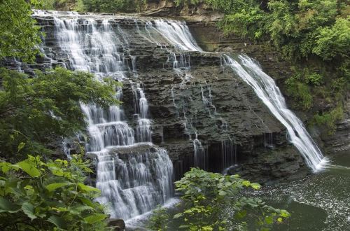 A serene waterfall cascading over rocky cliffs, surrounded by lush greenery and reflecting in a calm pool below.