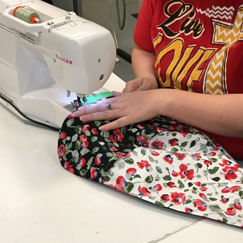 A person sewing a floral fabric with a sewing machine, focusing on the stitching process.