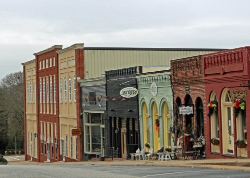 A row of historic brick buildings with shops, some decorated for the holidays, under a cloudy sky.