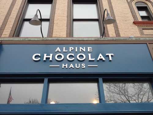 Sign for "Alpine Chocolat Haus" on a blue storefront with decorative lighting above.