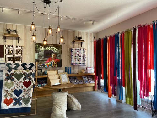 A cozy quilt shop featuring colorful fabric rolls, quilts on display, and warm lighting.