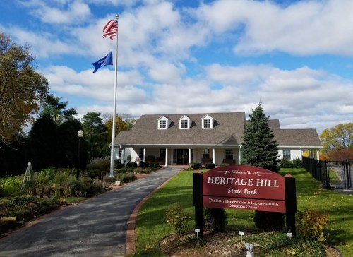 A welcoming entrance to Heritage Hill State Park, featuring a flagpole, sign, and a landscaped pathway.