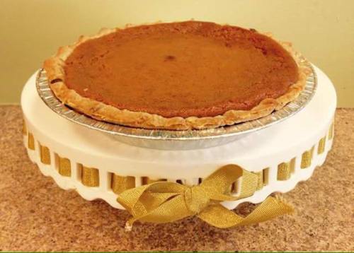 A pumpkin pie on a decorative white cake stand with a gold ribbon.