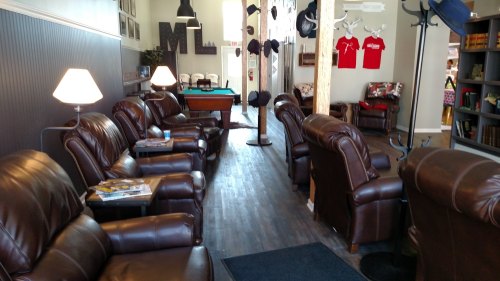 Cozy lounge with brown leather chairs, a pool table, and hats hanging on a post in a well-lit space.