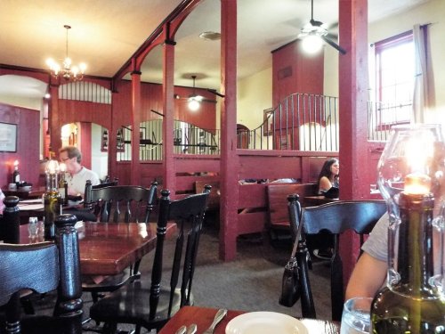 Cozy restaurant interior with wooden tables, red walls, and booths; diners enjoying meals in a warm atmosphere.