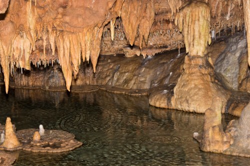 Stalactites and stalagmites in a cave, with a calm water surface reflecting the formations.