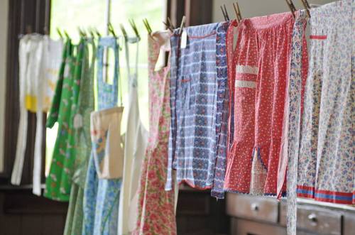 Colorful aprons hanging on a clothesline indoors, showcasing various patterns and designs.