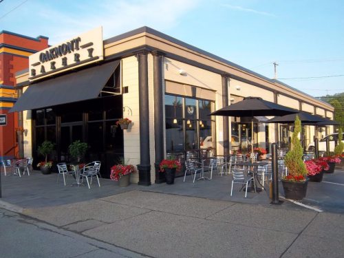 Exterior of Oakmont Bakery with outdoor seating, planters, and umbrellas on a sunny day.