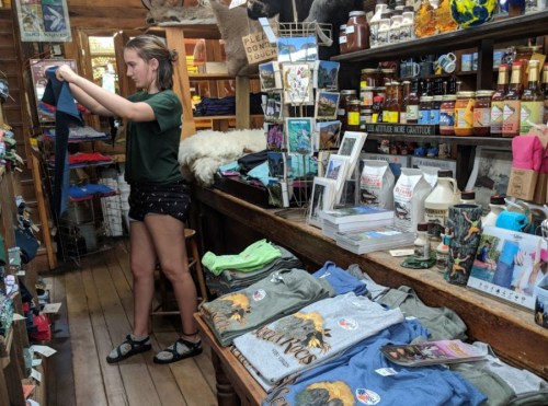 A young woman organizes clothing in a cozy shop filled with various merchandise and souvenirs.