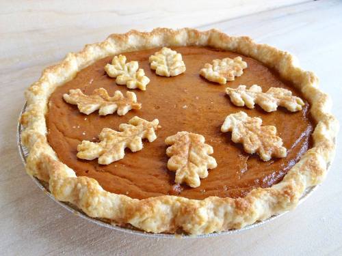 A pumpkin pie with a golden crust, topped with decorative leaf-shaped pastry pieces.