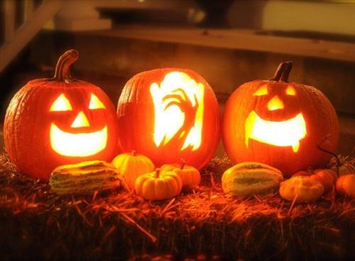 Three carved pumpkins with glowing faces, surrounded by small gourds, on a bed of hay. Perfect for Halloween decor.