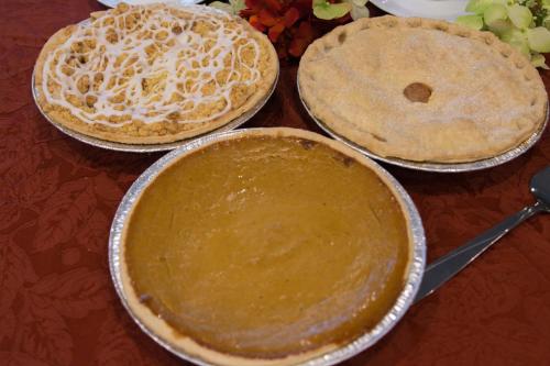 Three pies on a table: a pumpkin pie, a fruit pie with a lattice top, and a pie with a smooth, glazed topping.