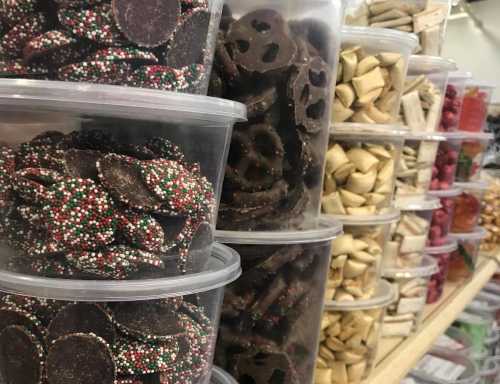 A display of various candies and snacks in clear containers, including chocolate discs, pretzels, and colorful treats.