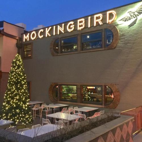 Exterior of a restaurant named "Mockingbird," featuring festive lights and a decorated Christmas tree.