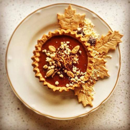 A decorative tart with a chocolate filling, topped with nuts and surrounded by pastry leaves on a white plate.