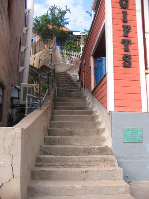 A steep, concrete staircase leads up between buildings, with greenery visible at the top and a sign for "Gifts" on the right.
