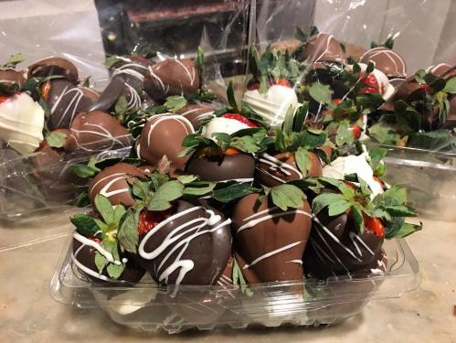 A tray of chocolate-covered strawberries, drizzled with white chocolate and garnished with green leaves.