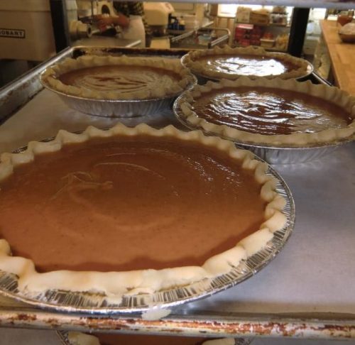 Four unbaked pies in metal pans, with various fillings, on a baking tray in a kitchen.