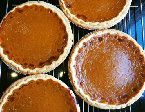 Four freshly baked pumpkin pies cooling on a wire rack.
