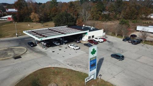 Aerial view of a gas station with multiple cars parked and a large sign in front, surrounded by trees and open land.