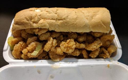 A sandwich filled with crispy fried shrimp and lettuce, served in a white takeout container.