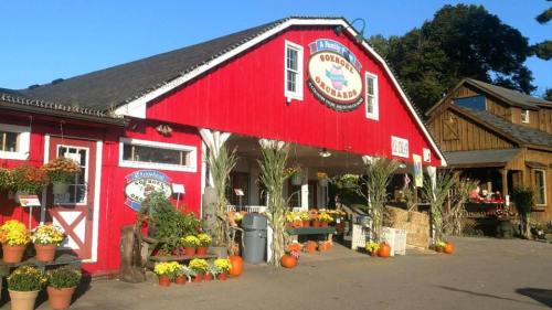 A red barn-style building with flowers, pumpkins, and autumn decorations outside, set in a rural landscape.